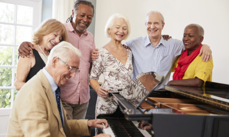 group of elderly huddled close to an elderly man playing a piano