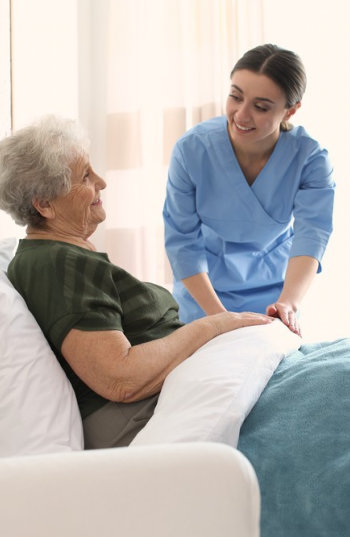 female aide smiling at an elderly woman laying in her bed