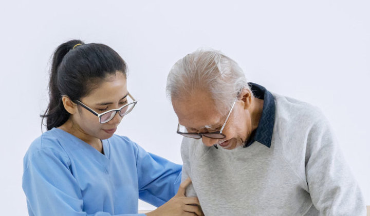 female aide guiding an elderly man in walking