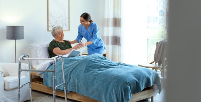 female aide giving a glass of water to an elderly woman in bed
