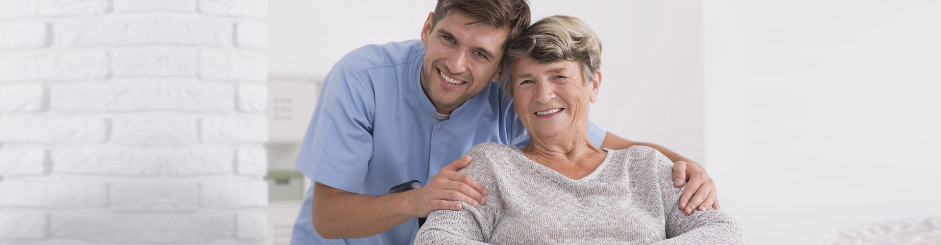 male aide with an elderly woman in wheelchair smiling