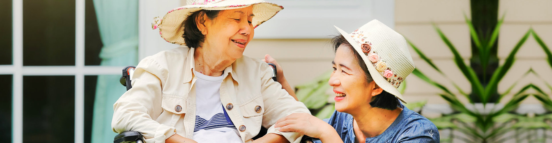 female aide and elderly woman in wheelchair smiling wearing hats